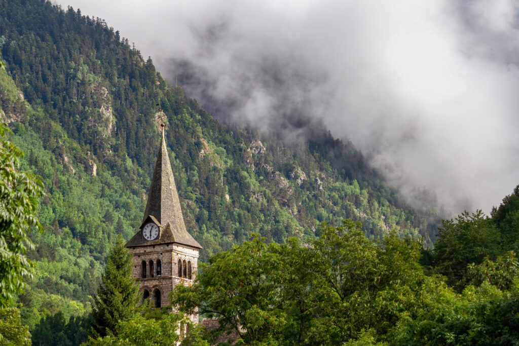 Bell Tower With A Clock In A Mountain Village. Clouds Cover A Hi